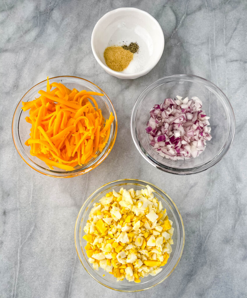 shredded cheese, onions, chopped boiled eggs, and seasoning in glass bowls