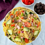 spaghetti salad in a white bowl with tomatoes and olivess
