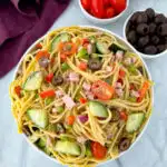 spaghetti salad in a white bowl with tomatoes and olivess