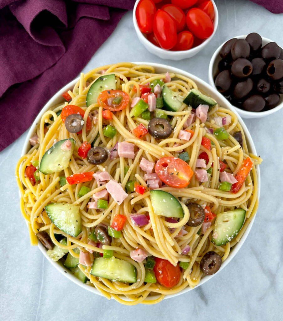 spaghetti salad in a white bowl with tomatoes and olivess