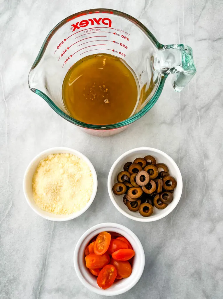 Italian dressing, Parmesan cheese, olives, and tomatoes in separate bowls