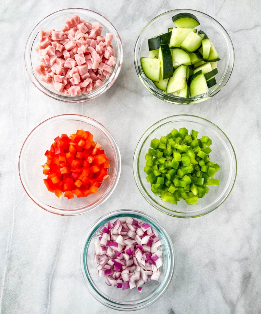 chopped ham, cucumbers, red peppers, green peppers, and red onions in separate bowls