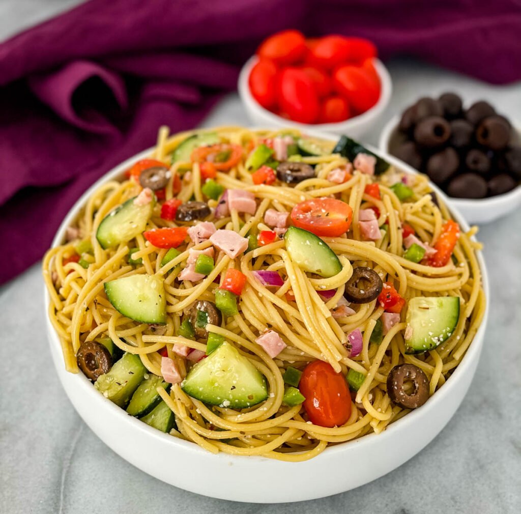 spaghetti salad in a white bowl with tomatoes and olivess