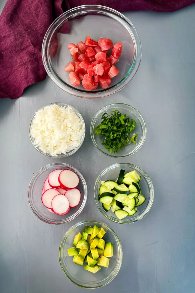 raw ahi tuna, white rice, fresh avocado, fresh radishes, chopped green onions, and cucumbers in separate bowls
