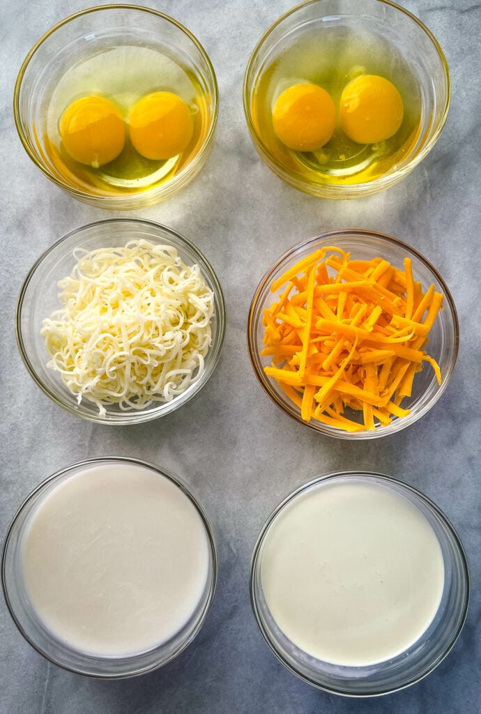 raw eggs, shredded cheese, almond milk, and heavy cream in separate glass bowls