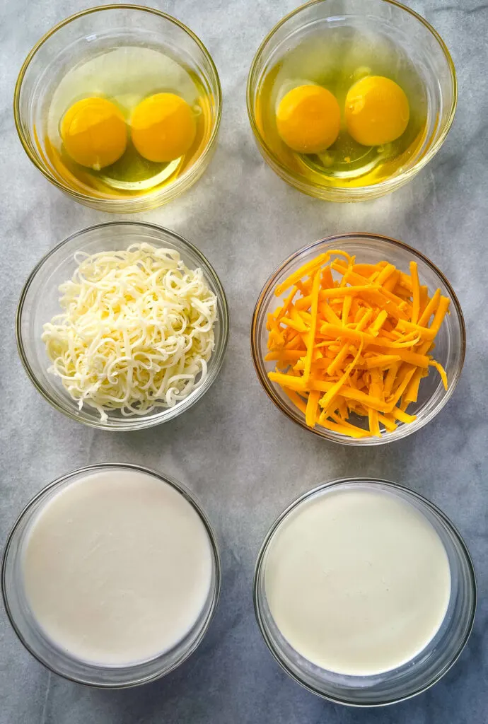 raw eggs, shredded cheese, almond milk, and heavy cream in separate glass bowls