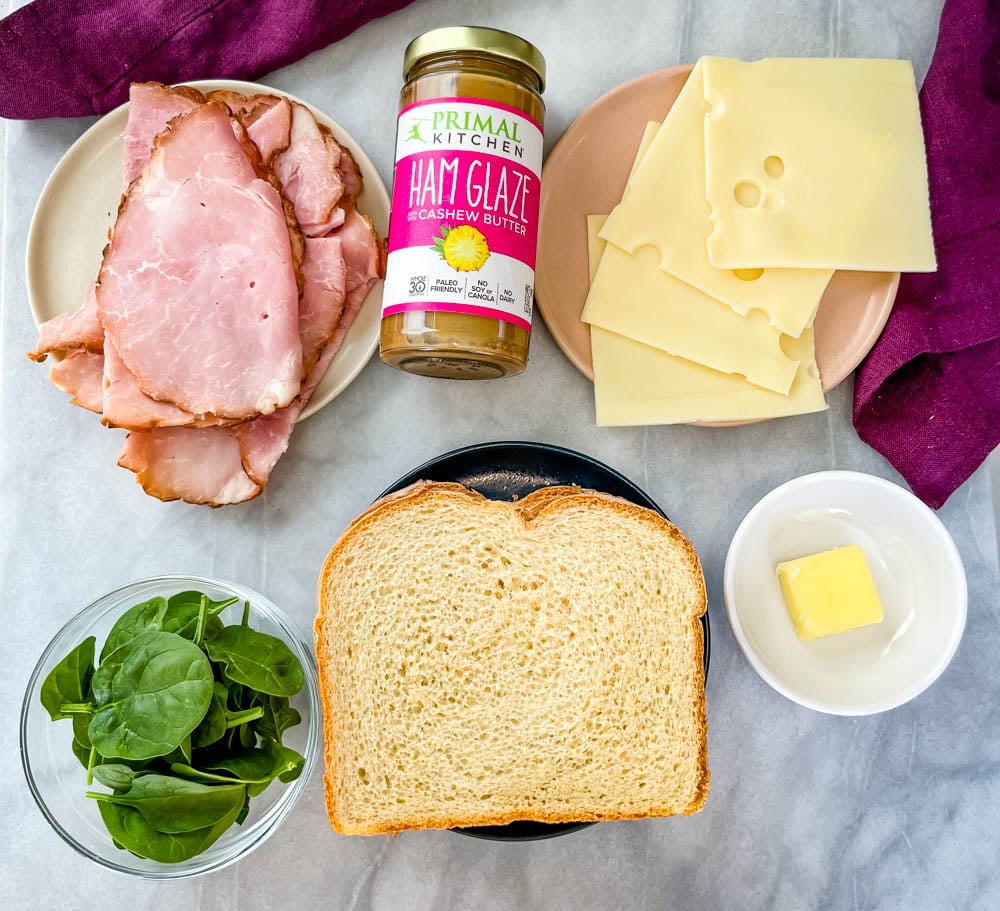 sliced ham, swiss, 2 slices of bread, spinach, and butter on separate plates