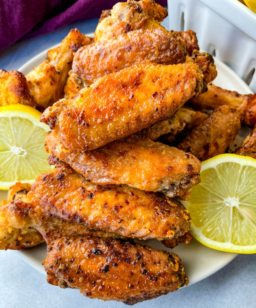 lemon pepper chicken wings on a white plate with fresh lemons