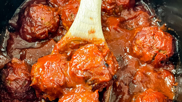 BBQ meatballs in a slow cooker with a wooden spoon