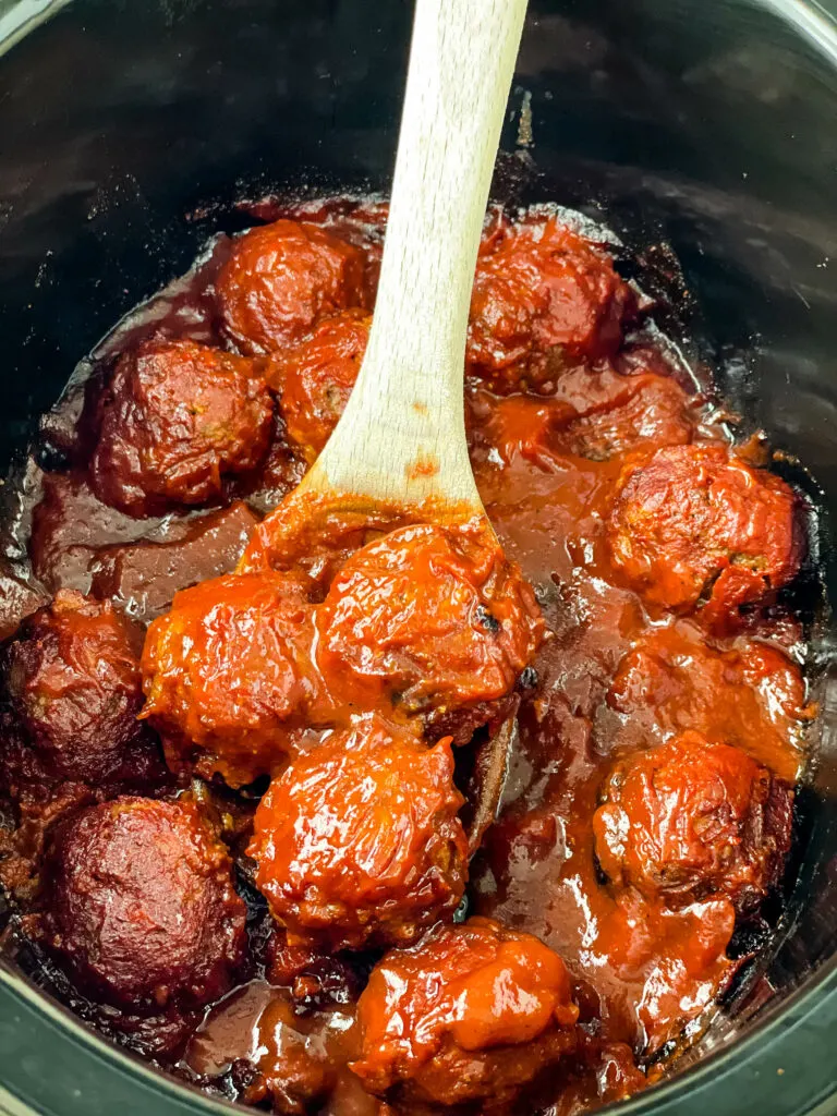 BBQ meatballs in a slow cooker with a wooden spoon