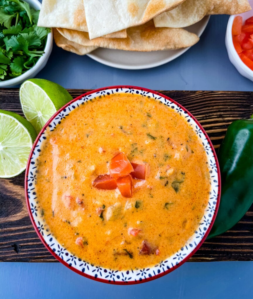 queso cheese dip in a red bowl with a plate of chips