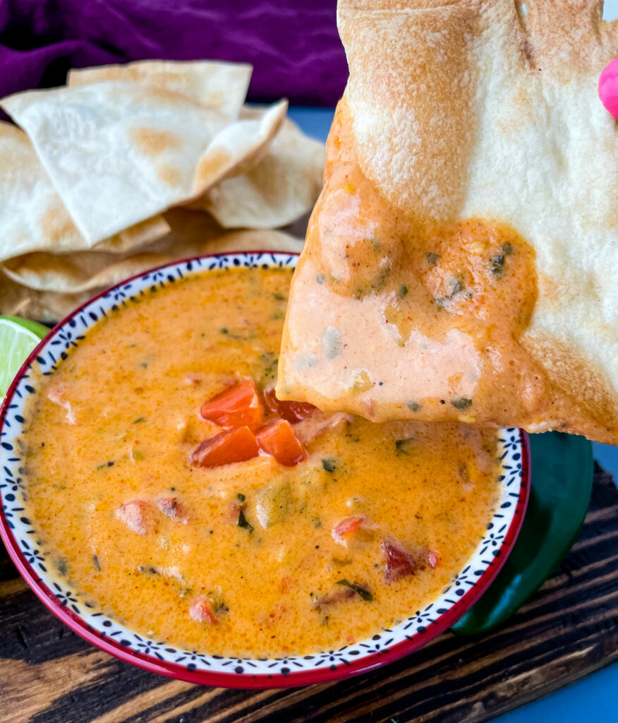 person holding a chip with homemade queso cheese dip