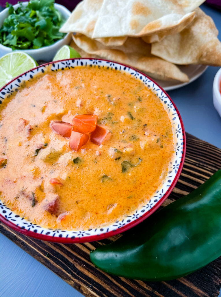 queso cheese dip in a red bowl with a plate of chips