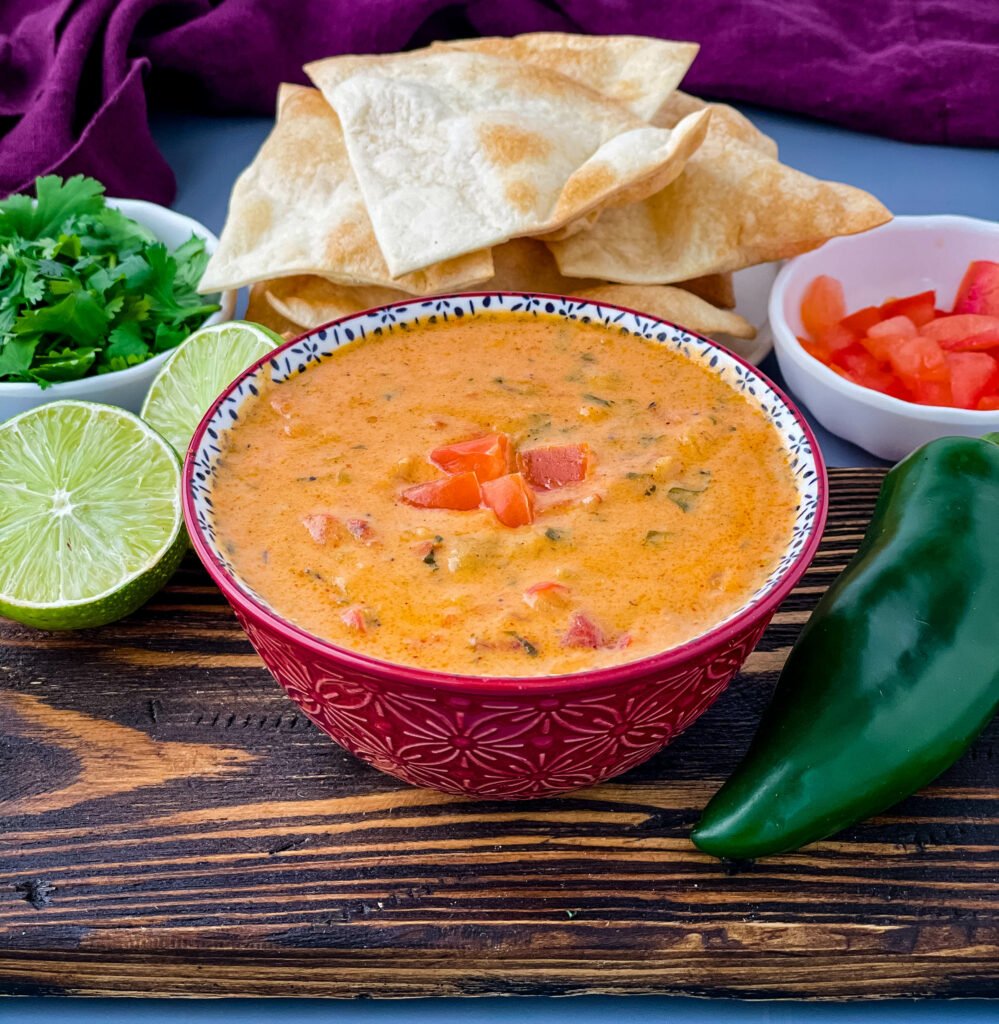 queso cheese dip in a red bowl with a plate of chips