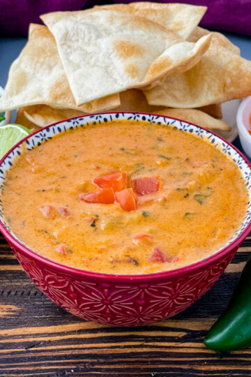 queso cheese dip in a red bowl with a plate of chips