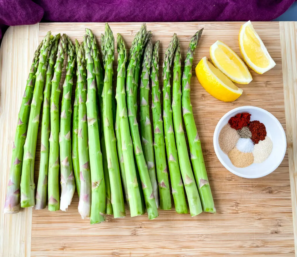 raw asparagus on a wooden cutting board with lemons and bbq seasoning