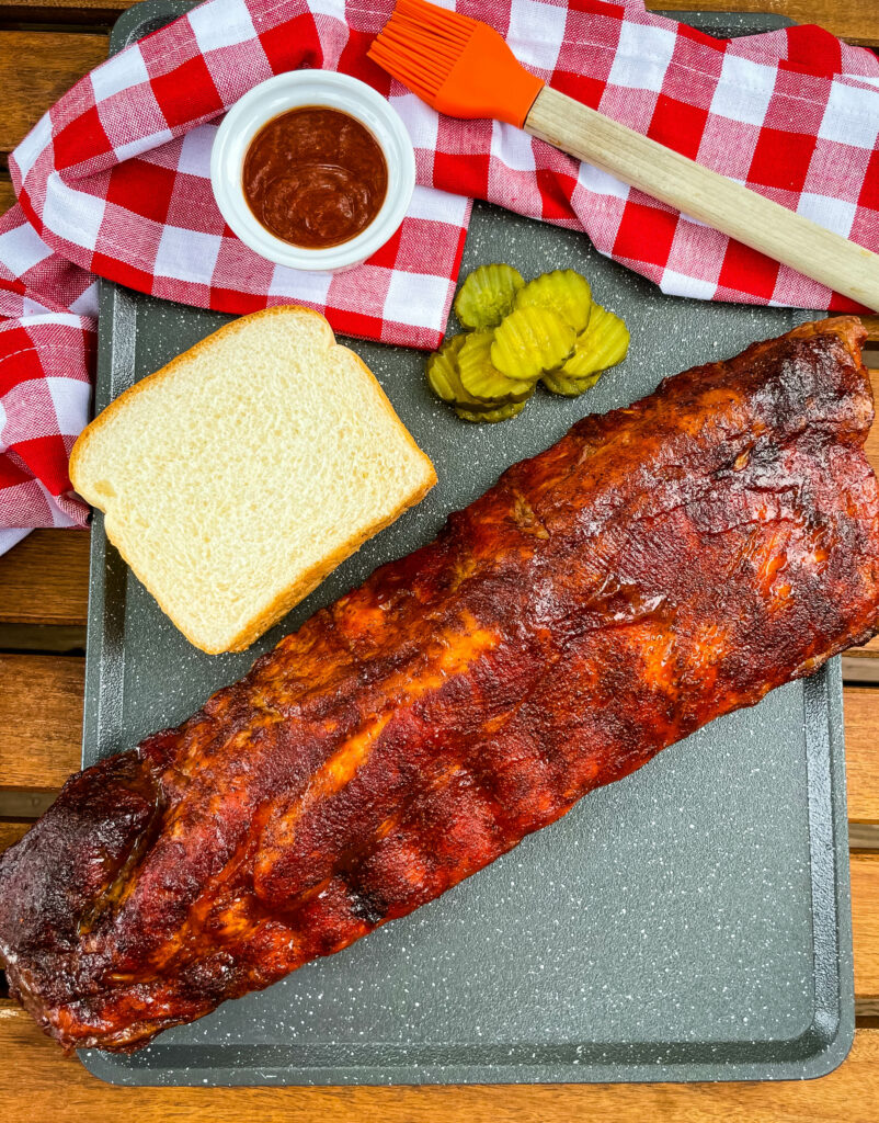 baby back ribs on a plate with bread, BBQ sauce, and pickles