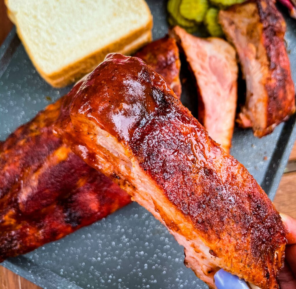 person holding baby back rib with BBQ sauce