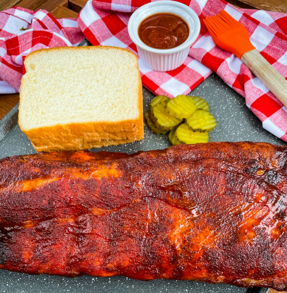 baby back ribs on a plate with bread, BBQ sauce, and pickles