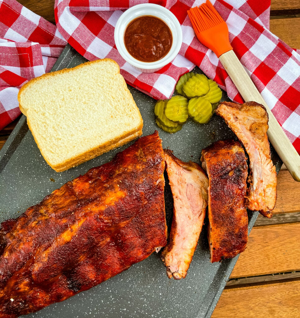 baby back ribs on a plate with bread, BBQ sauce, and pickles