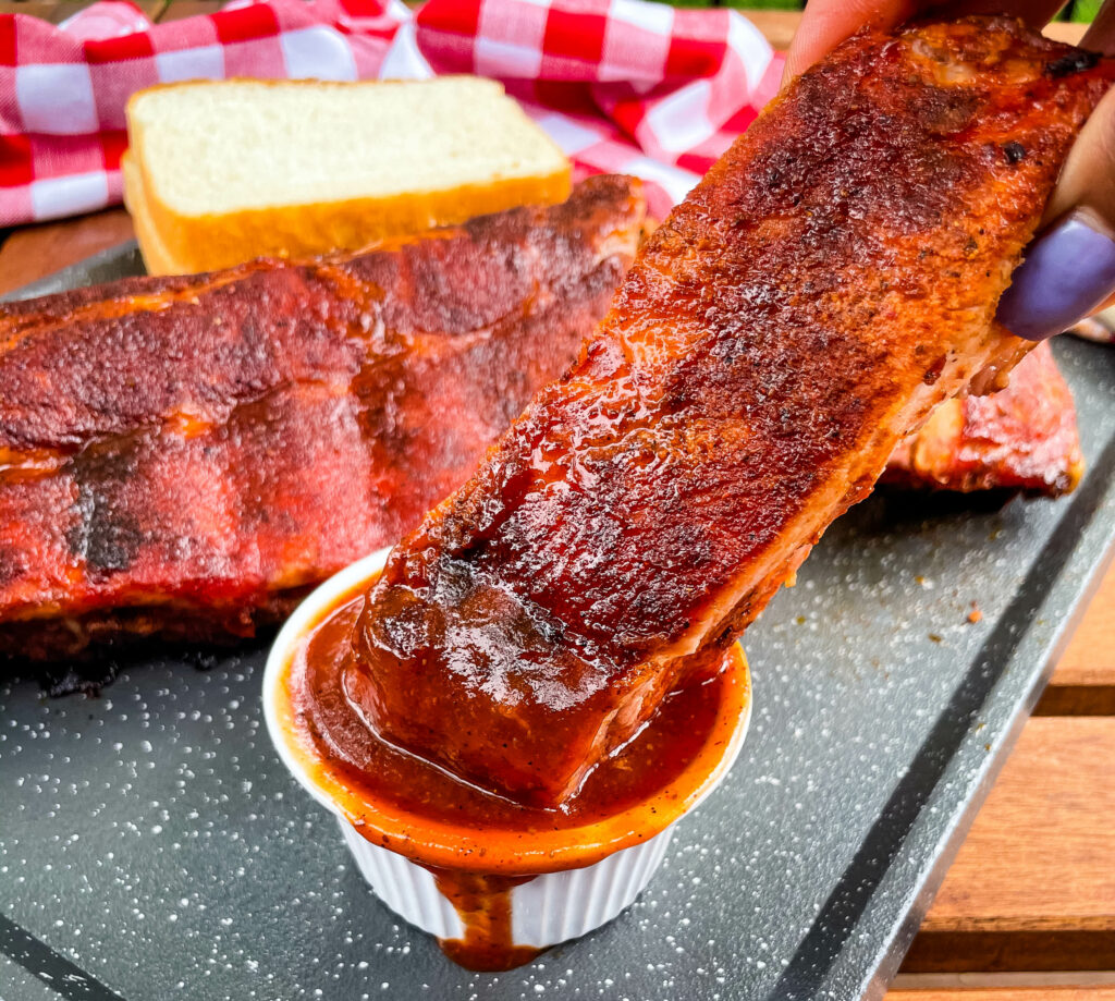 person holding baby back rib with BBQ sauce