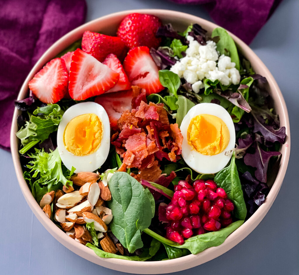 healthy breakfast salad in a bowl with bacon, eggs, and strawberries