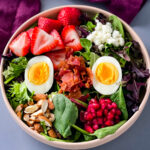 healthy breakfast salad in a bowl with bacon, eggs, and strawberries