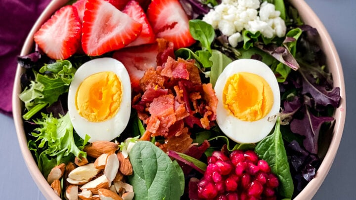 healthy breakfast salad in a bowl with bacon, eggs, and strawberries