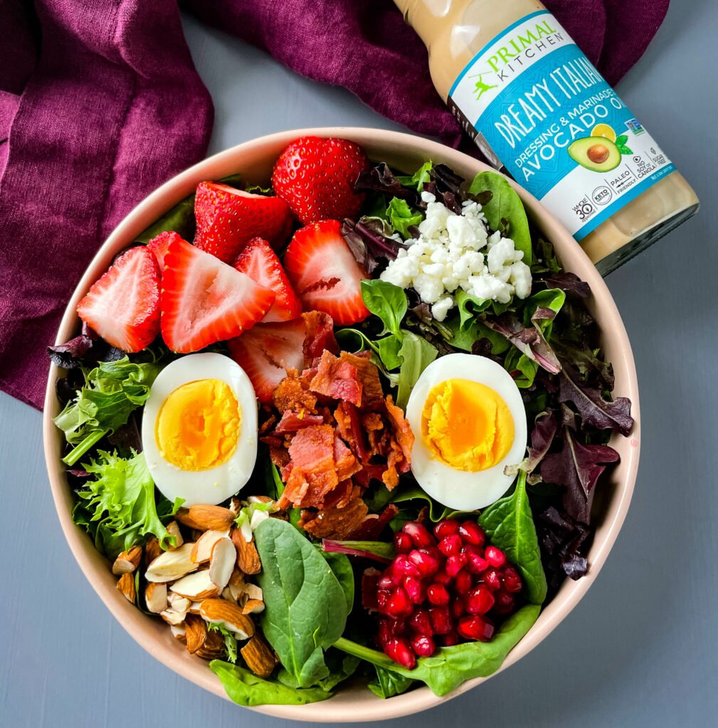 healthy breakfast salad in a bowl with bacon, eggs, and strawberries