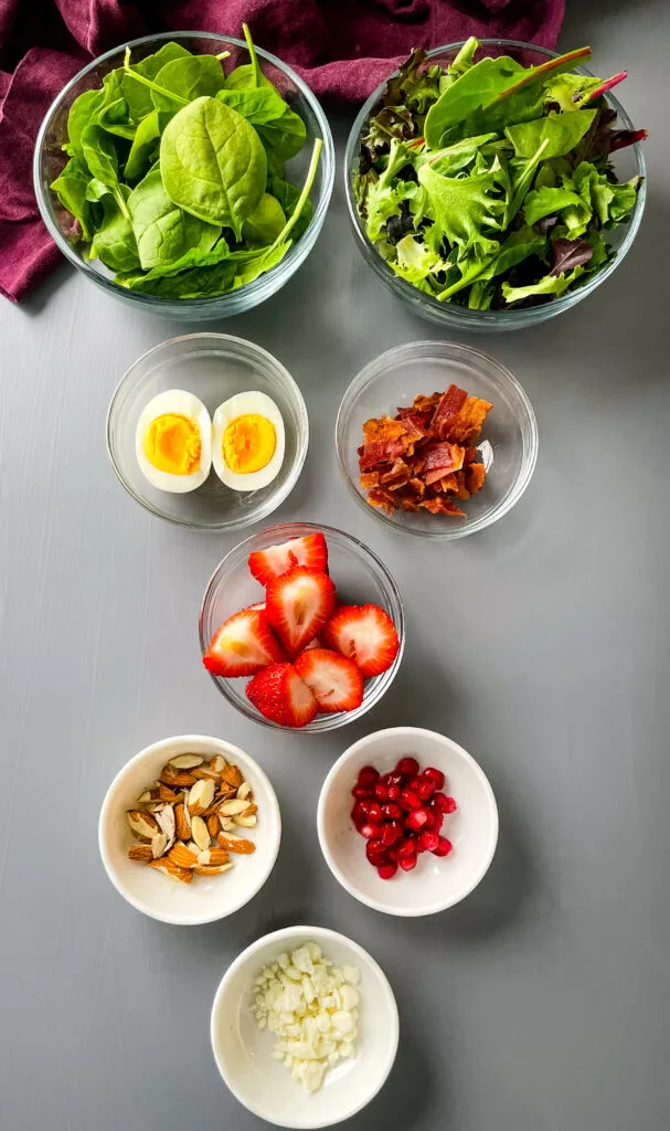 fresh spinach, fresh mixed greens, boiled eggs, pomegrante seeds, feta cheese, strawberries, and almonds in separate bowls