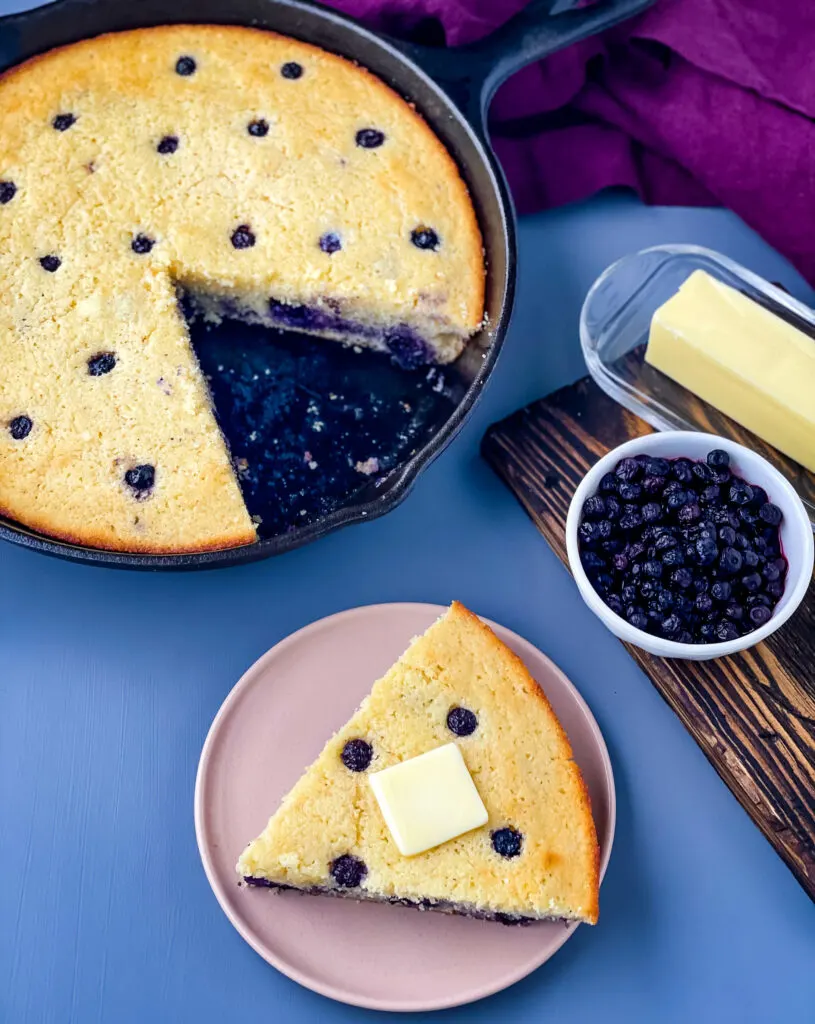 a slice of homemade blueberry cornbread on a plate with a pan of cornbread