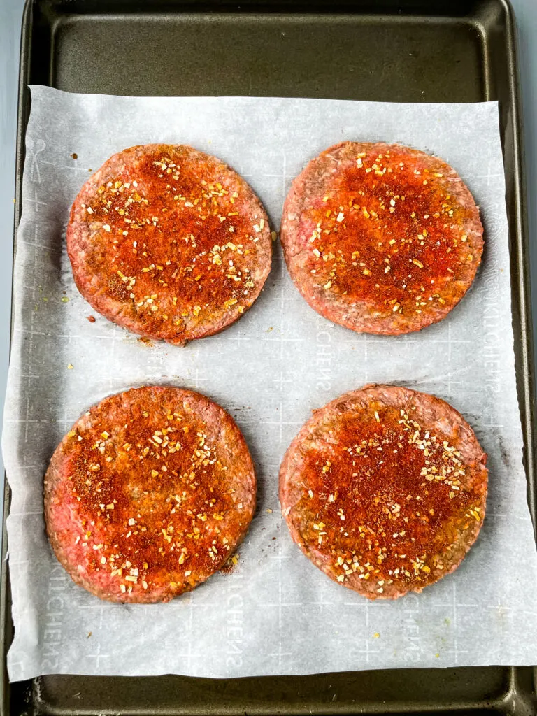 raw seasoned hamburger patties on a sheet pan