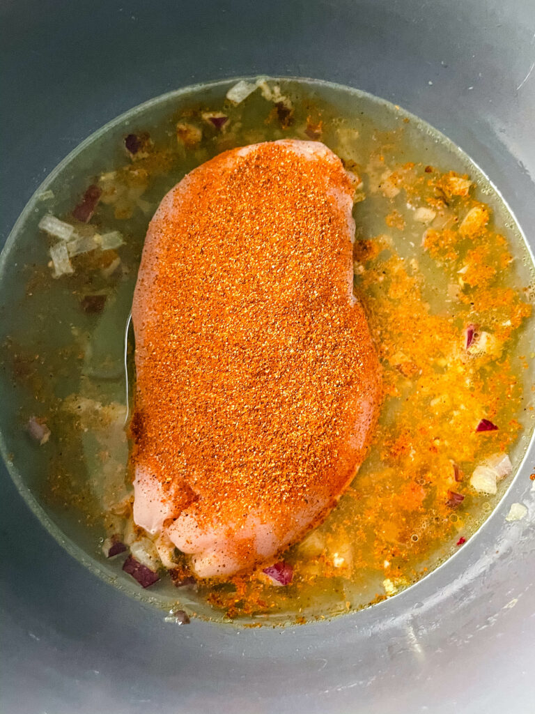 raw chicken in an Instant Pot with broth and seasoning