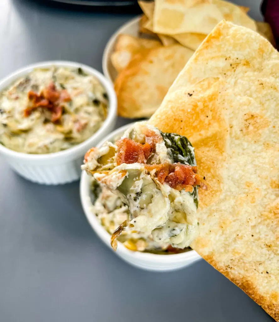person holding bacon spinach artichoke dip on a chip