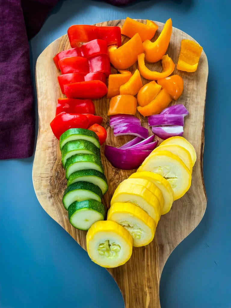 chopped peppers, zucchini, squash, and red onions on a cutting board