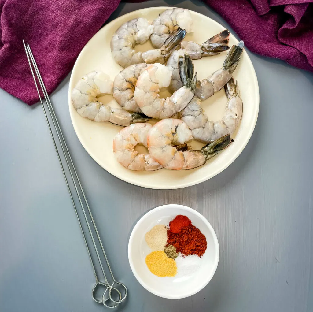 raw shrimp on a plate with skewers and BBQ seasoning in a bowl