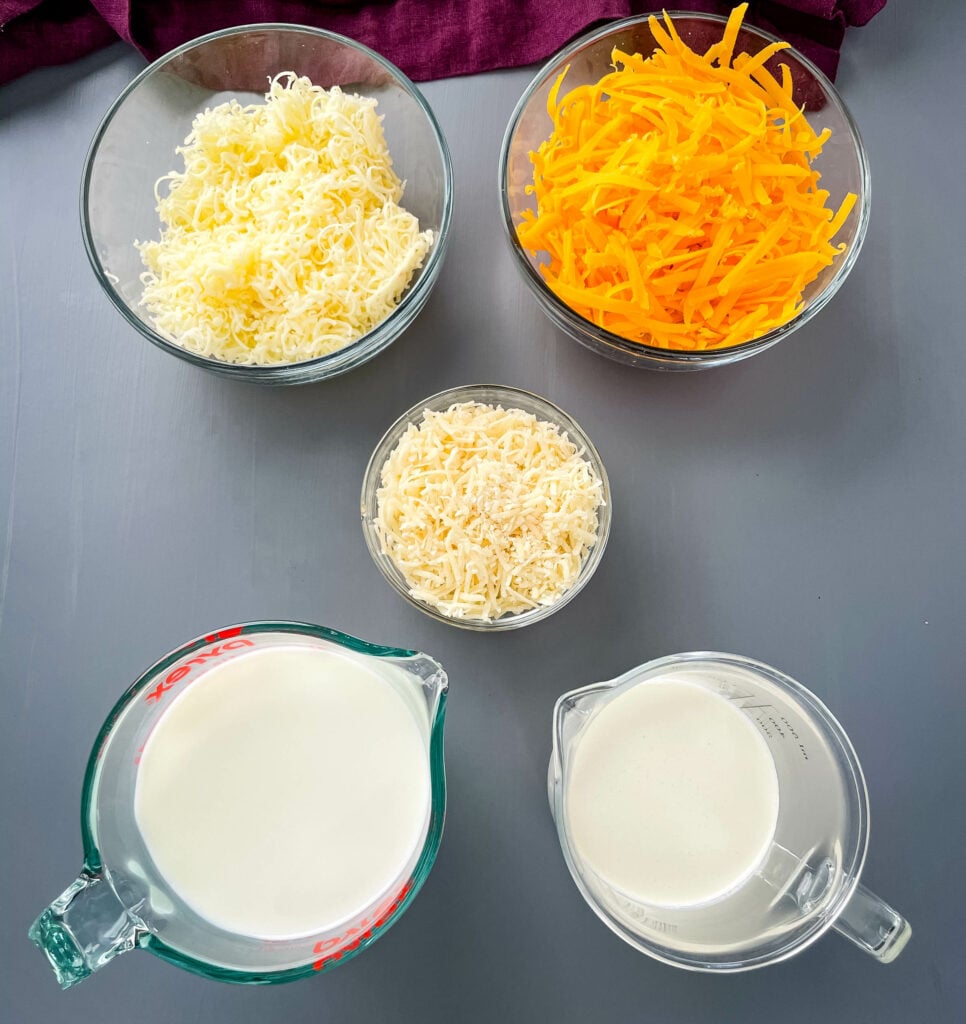 shredded cheddar cheese and parmesan in separate bowls along with milk and heavy cream