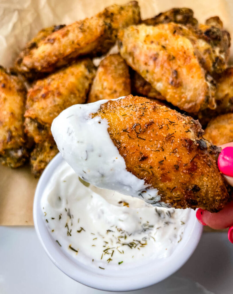 person holding ranch chicken wing dipped in ranch dressing
