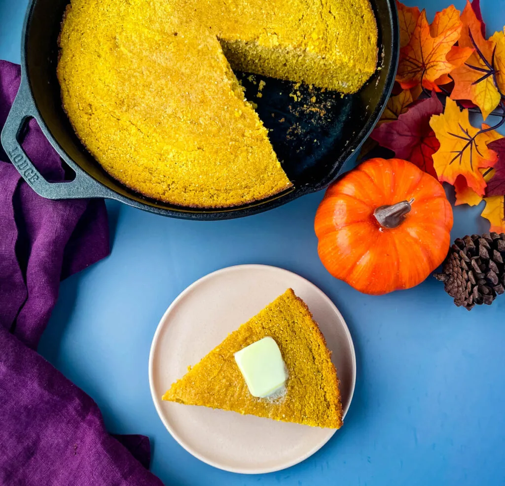 pumpkin cornbread on a plate with pumpkin cornbread in a cast iron skillet