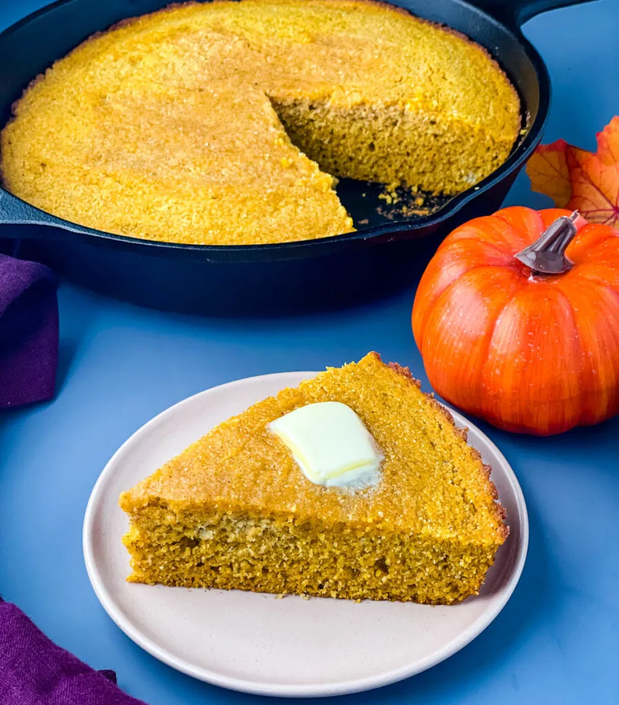 pumpkin cornbread on a plate with pumpkin cornbread in a cast iron skillet