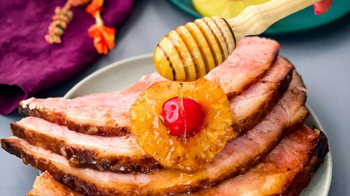 ham sliced on a plate with pineapples, cherries, and drizzled in honey