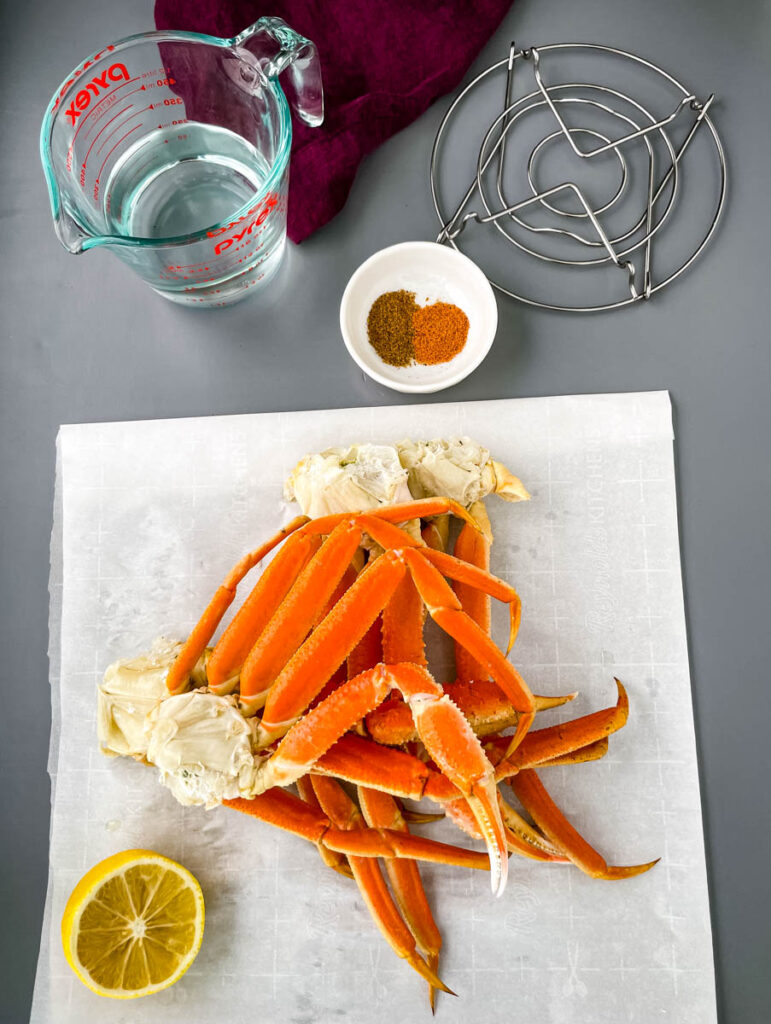 fresh crab legs, spices, water, lemon, and trivet on a flat surface