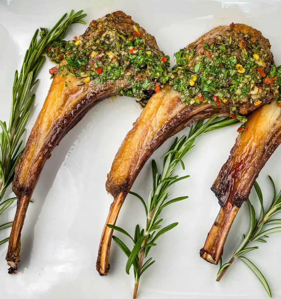 air fryer lamb chops on a white plate with rosemary and chimichurri sauce
