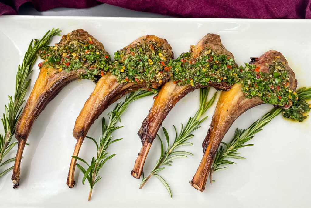 air fryer lamb chops on a white plate with rosemary and chimichurri sauce