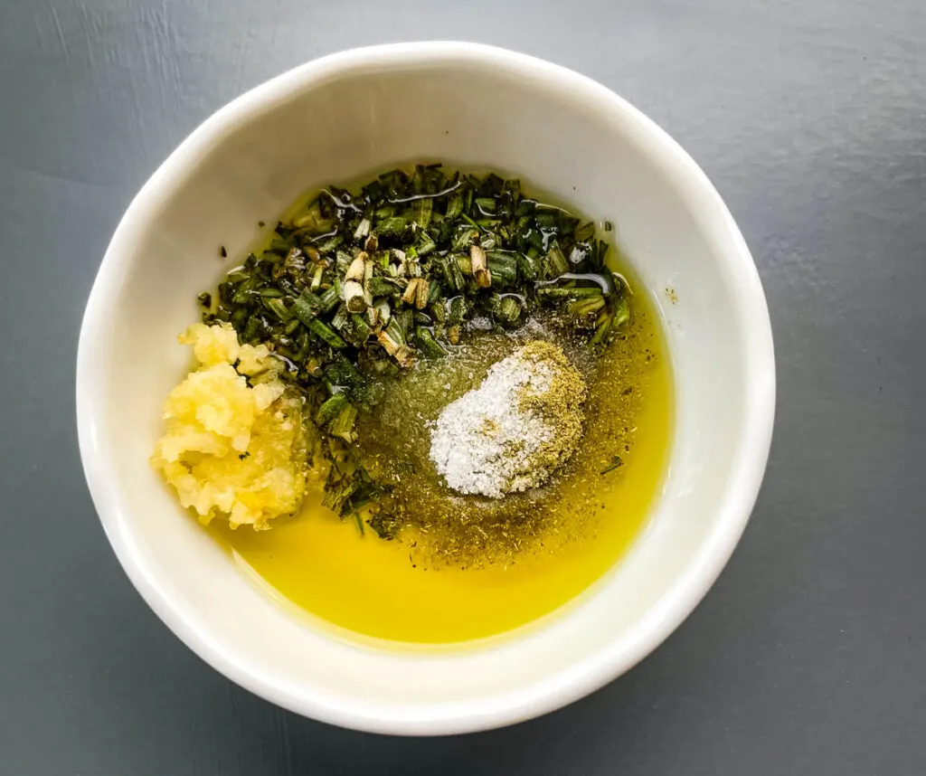 garlic, olive oil, rosemary, and oregano in a white bowl