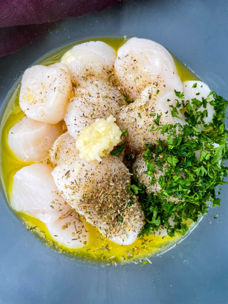 raw scallops in a glass bowl with melted butter, olive oil, parsley, and garlic