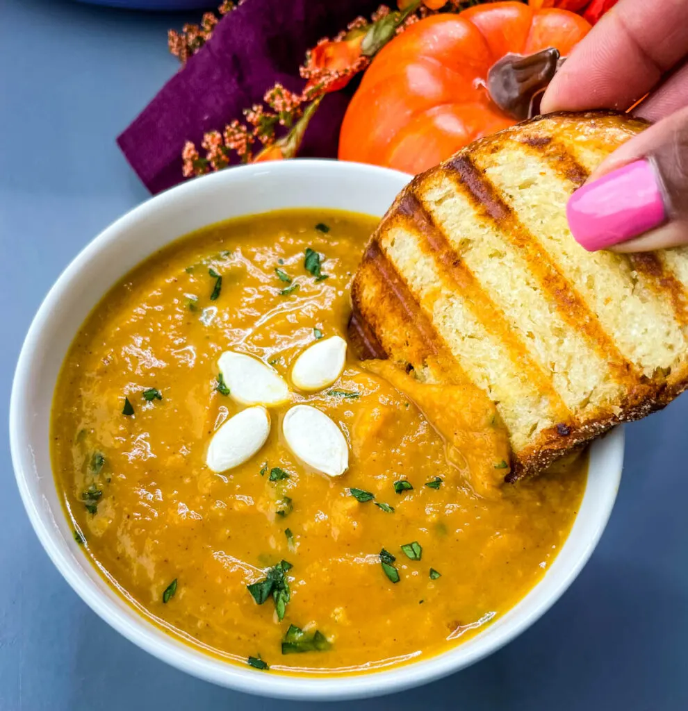 person dipping a slice of bread in a bowl of canned pumpkin soup