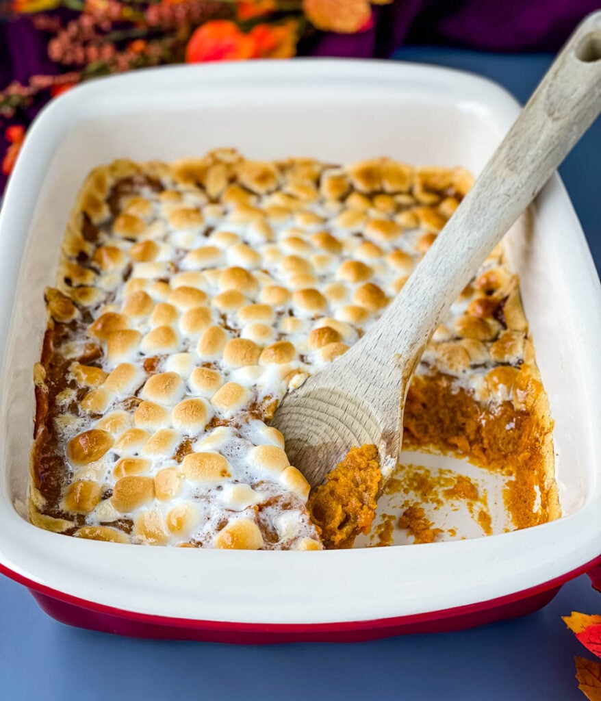 spoonful of sweet potato casserole with marshmallows in a red baking dish