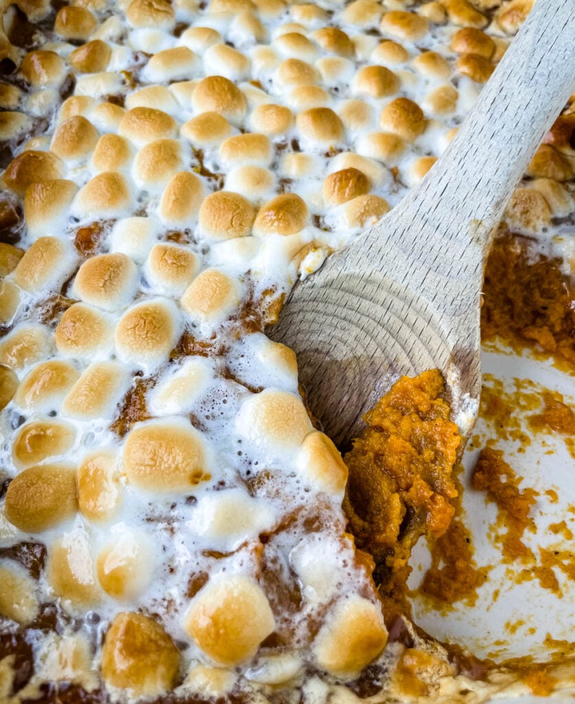 spoonful of sweet potato casserole with marshmallows in a red baking dish