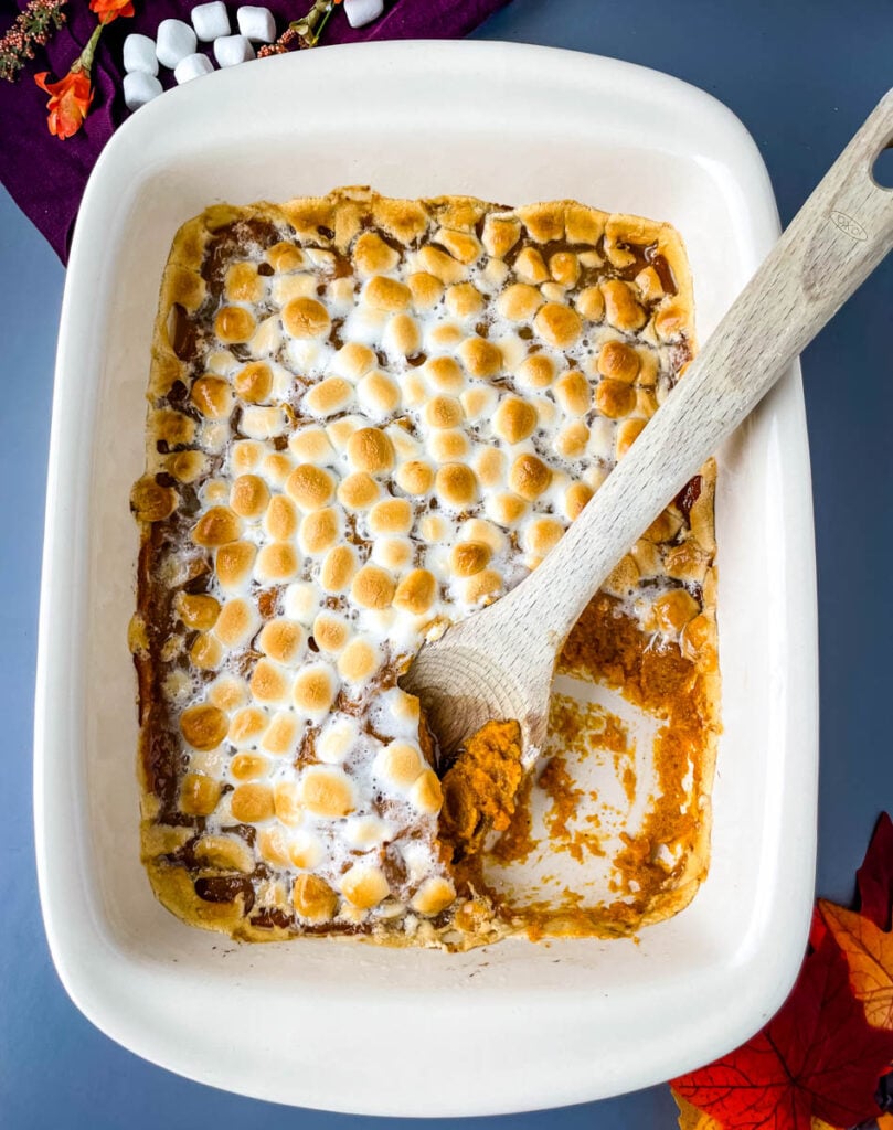 spoonful of sweet potato casserole with marshmallows in a red baking dish